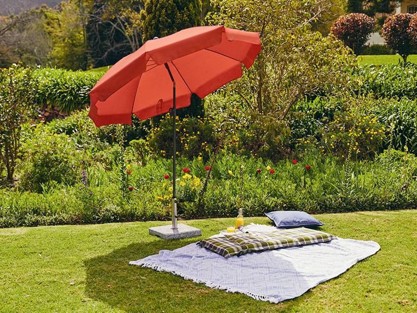 Roter Sonnenschirm und Picknickdecke in einem schönen Garten.