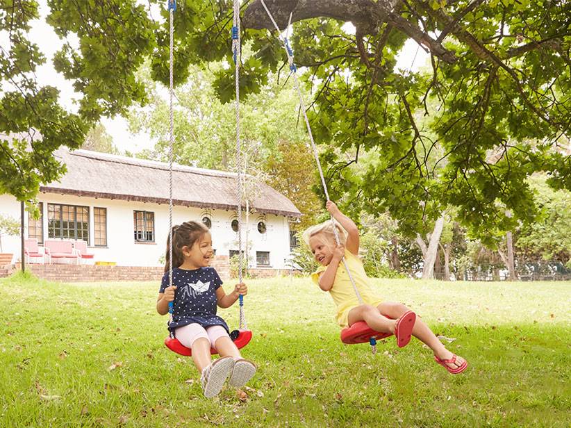 Kinder schaukeln auf roten Schaukeln, die an einem Baum hängen.