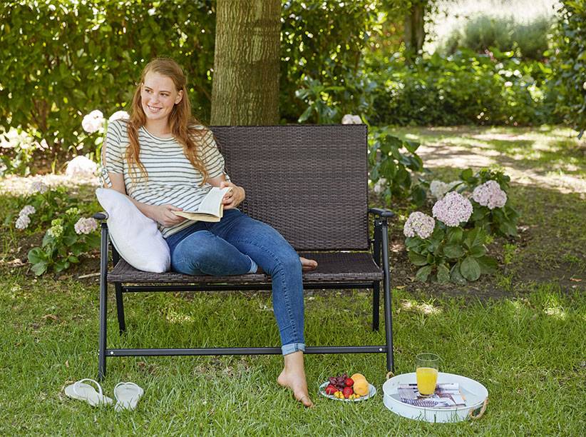 Frau entspannt sich auf einer Gartenbank aus Geflecht.