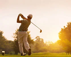 Golfer schlägt Ball im Sonnenuntergang.