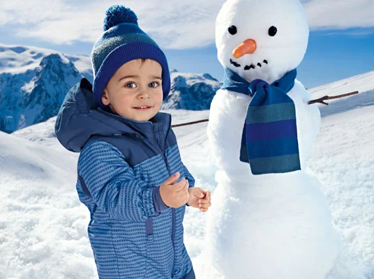 Baby-Winteroverall und Mütze neben einem Schneemann.