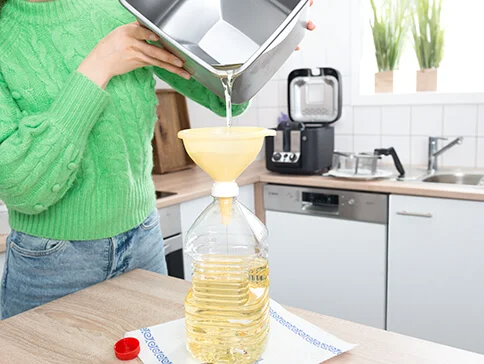 Frau gießt Öl aus einer Schüssel in eine Flasche mit einem Trichter.