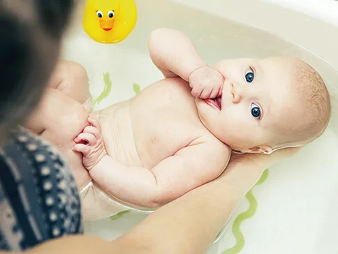 Baby im Bad, in den Armen eines Erwachsenen.