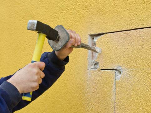 Hammer und Meißel werden an einer gelben Wand verwendet.
