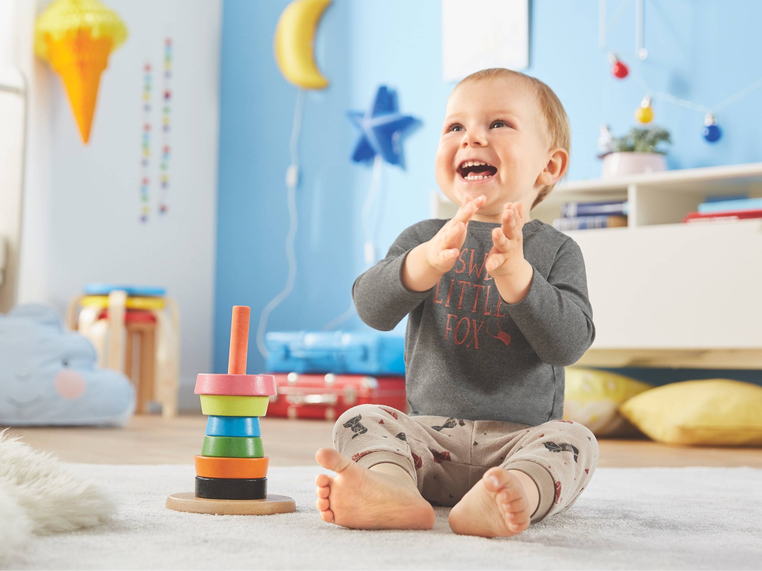 Baby spielt mit einem Holz-Stapelspielzeug und trägt süße Kleidung.