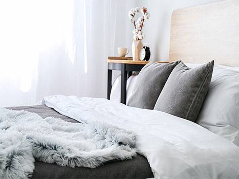 Weiche graue Decke und Kissen auf einem weißen Bett.