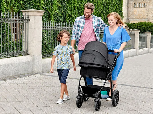 Familie spaziert mit Kinderwagen und Kind.