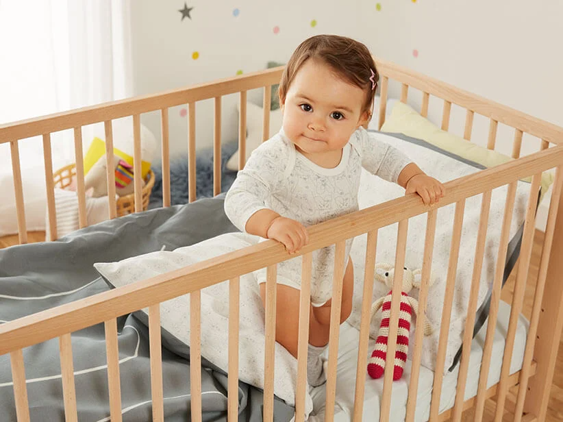 Baby im Holzbett, Babykleidung und Stofftier.