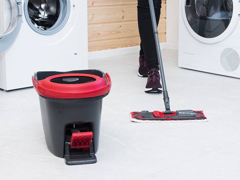 Vileda-Wischer und Eimer neben Waschmaschinen.