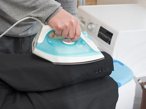 Eine Person bügelt einen dunklen Mantel mit einem Bügeleisen.