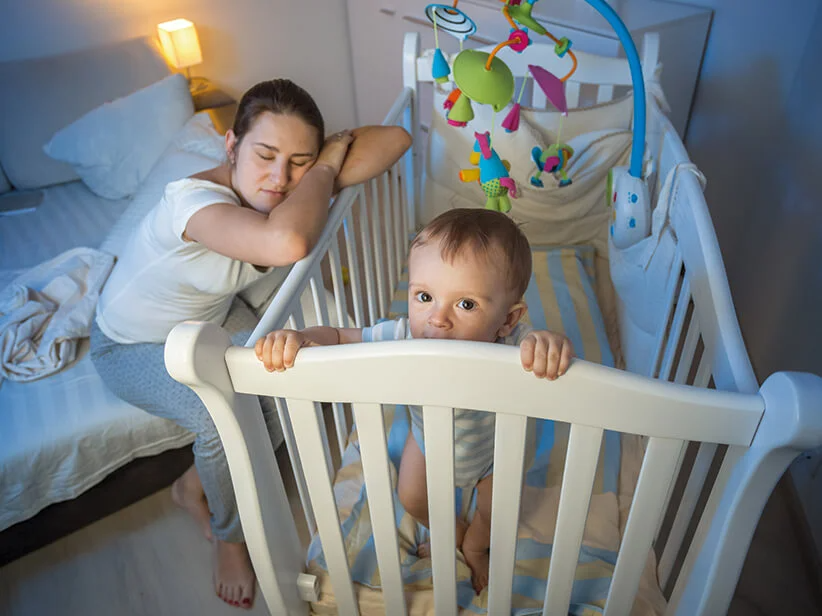 Mutter schläft neben Baby im Kinderbett.