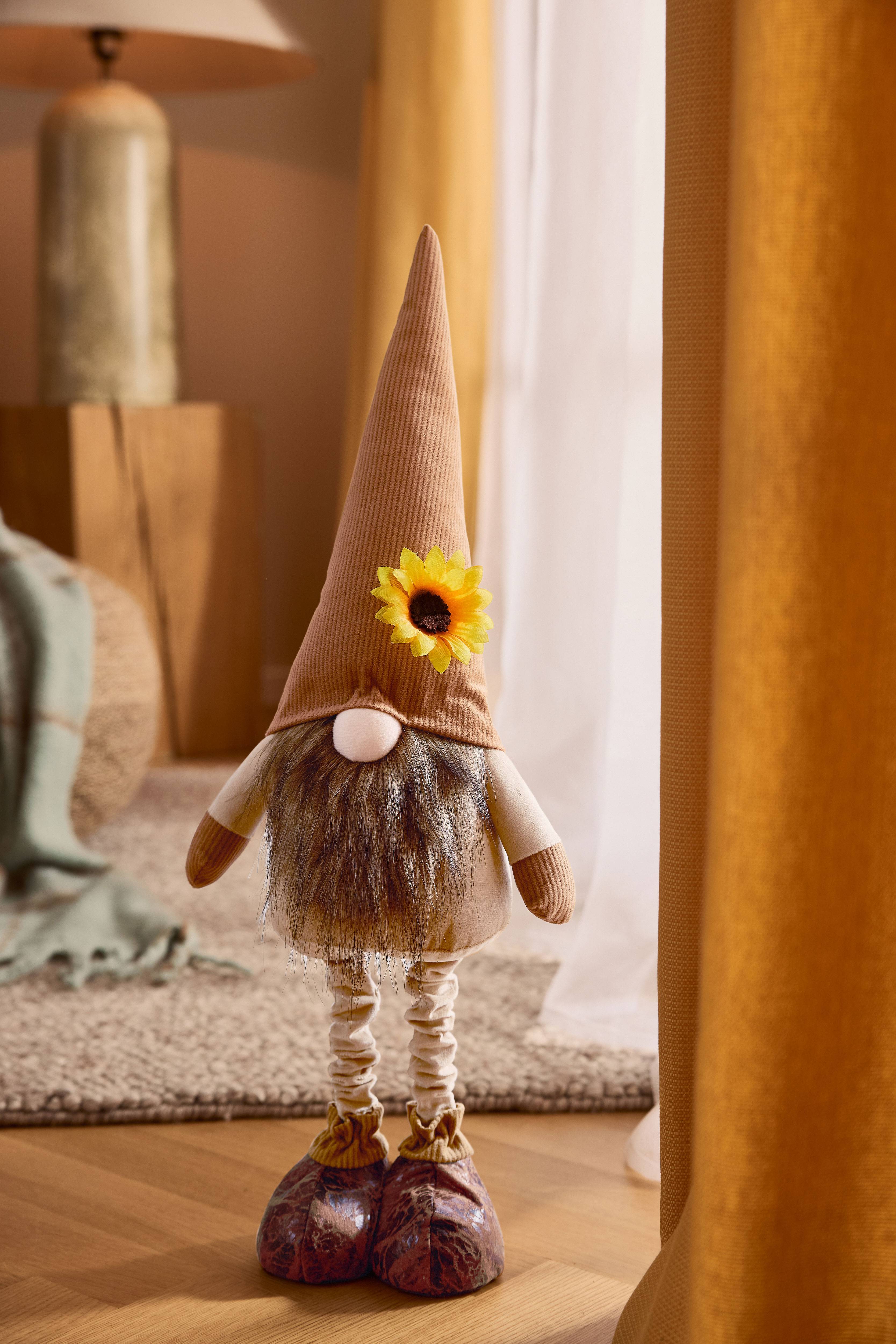 Plüsch-Gnom mit braunem Spitzhut, Bart und Sonnenblume, in gemütlicher Umgebung.