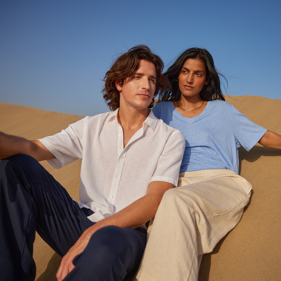 Zwei junge Menschen in der Wüste, tragen ein weißes Hemd und ein blaues T-Shirt, marineblaue und beige Hosen.