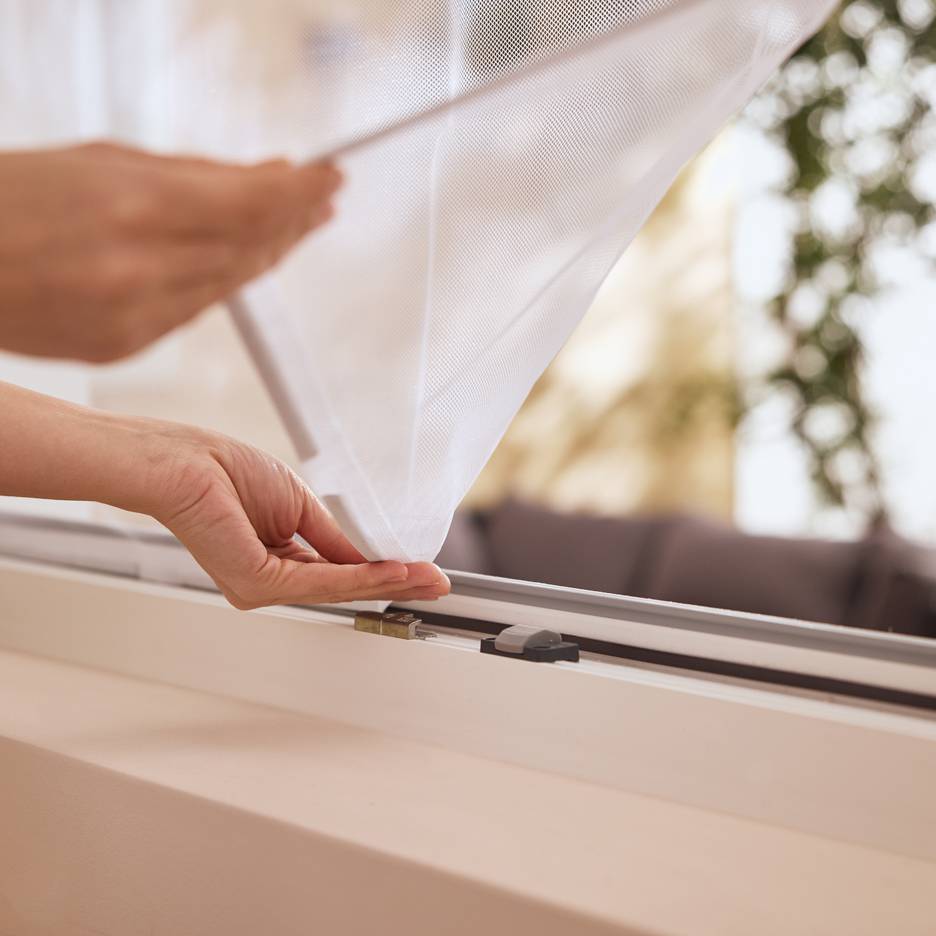 Hände installieren ein weißes Moskitonetz an einem Fenster