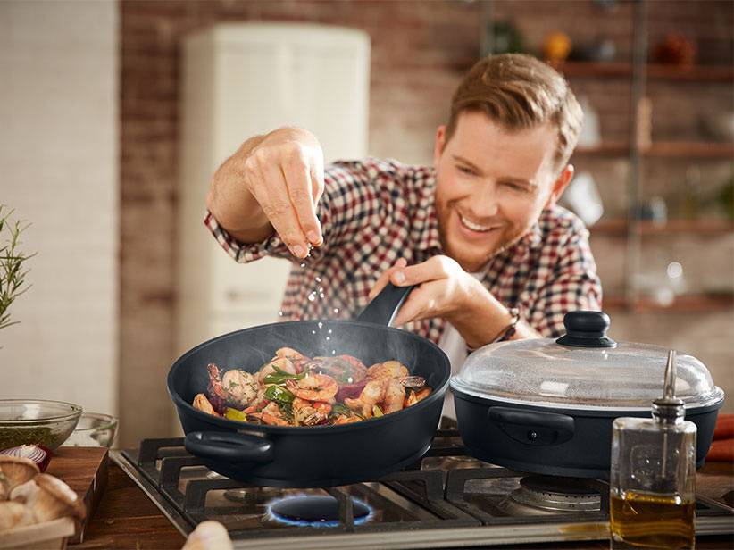 Mann kocht Essen in Pfanne und Topf.