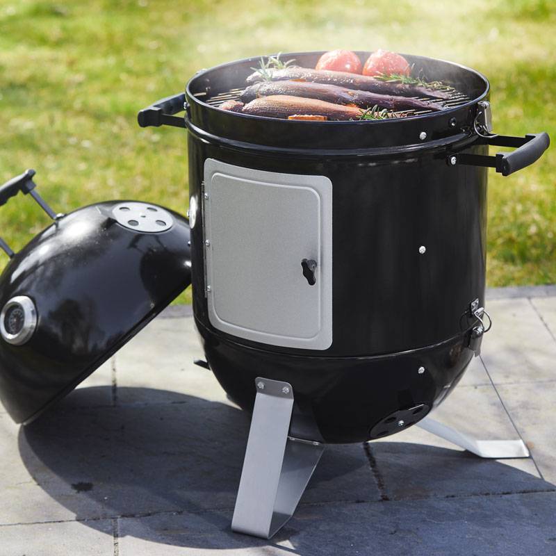 Schwarzer Fassgrill mit gegrilltem Fisch und Gemüse.