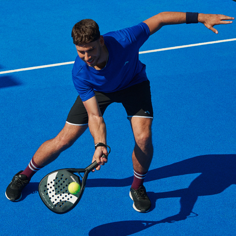 Mann in blauem T-Shirt und schwarzen Shorts spielt Padel mit Schläger und Ball.