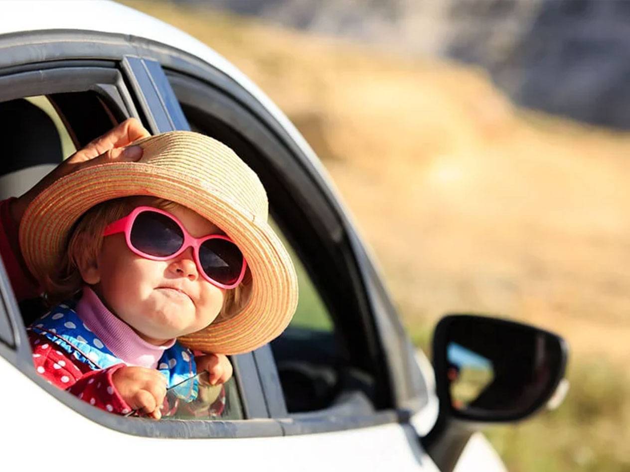 Kleinkind mit Sonnenhut und Sonnenbrille im Auto.