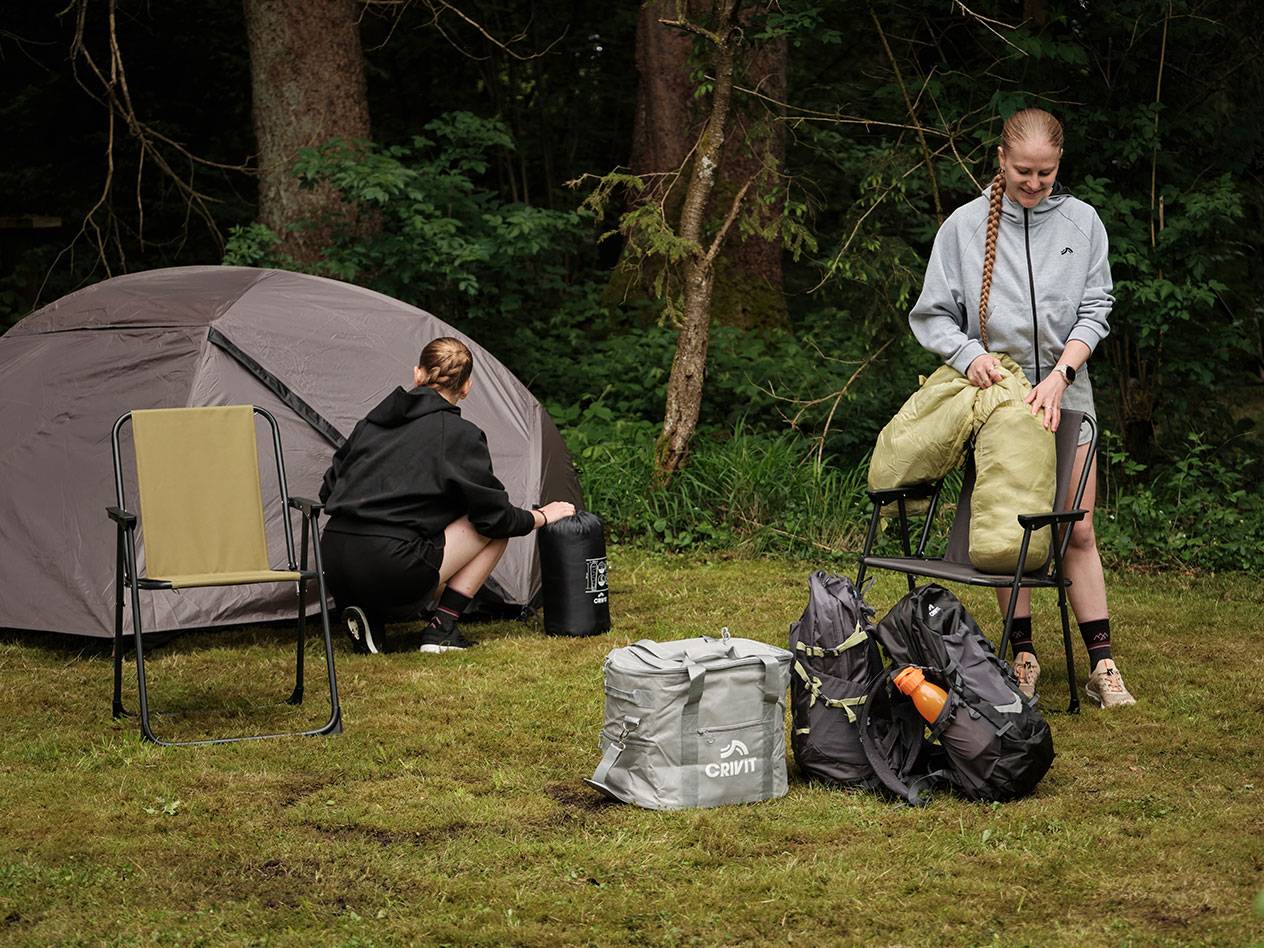 Zwei Personen packen Campingausrüstung aus, darunter eine Crivit Kühltasche und ein Zelt.