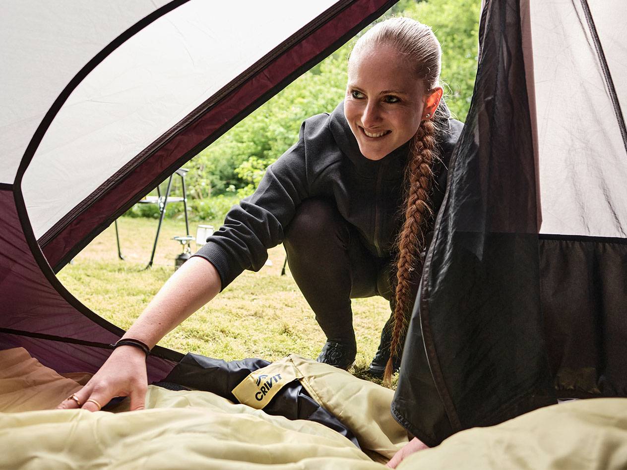 Eine Frau legt einen Crivit Schlafsack in ein Zelt.