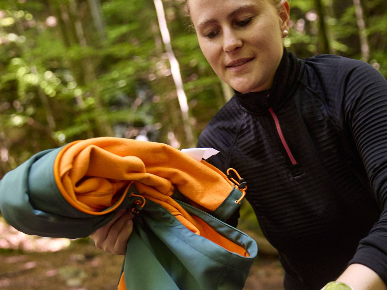 Frau in einem Wald faltet eine Sportjacke zusammen.